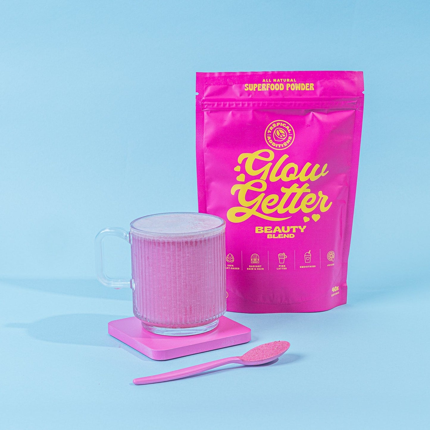 
                  
                    Beauty Boosting Superfood Blend | Glow Getter | Tropical Additions - packet next to pink latte and spoon with powder on.
                  
                